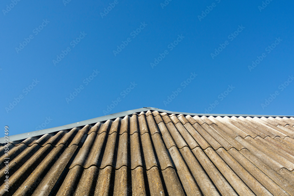 Old wavy slate roof against blue sky. Texture of old slate . Shed roof covered with old asbestos sheets. Texture of old roof, slate background.