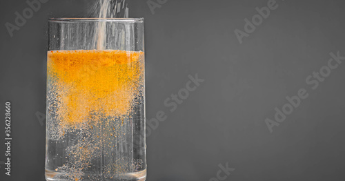 Powdered orange drink mix being poured into a clear glass of water photo