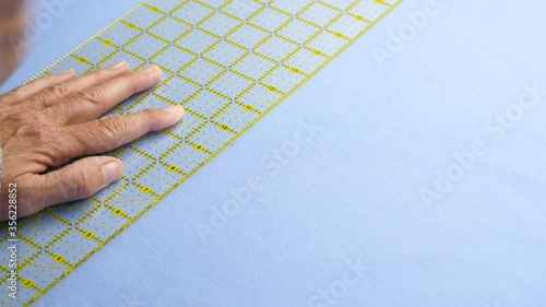 Female cuts blue cotton fabric using a yellow ruler to guide a rotary cutter on a green cutting mat 