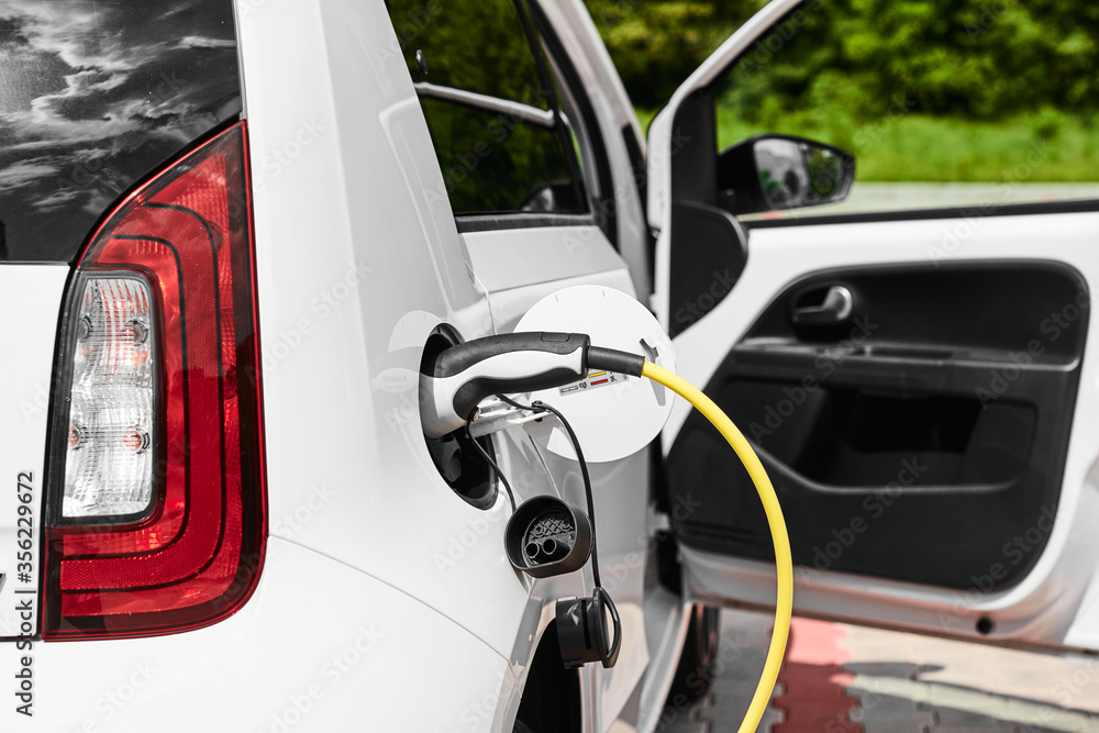 Yellow electric socket charging an electric car in the street. Power supply plugged into the electric automobile Yellow electric socket charging an electric car in the street. Power supply plugged into the electric automobile