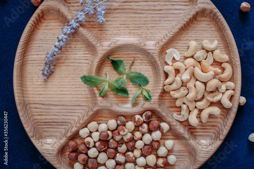 A round five sections wooden serving board with hazelnuts, cashews, branch of lavender and mint leaves  on a dark blue background photo