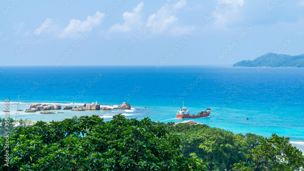 Panoramic view of famous granite rocks in blue sea at La Digue, Seychelles. orange cargo ship going to Praslin island