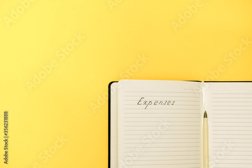 Expenses and budget planning concept. Top view of notepad with handwritten words Expenses on yellow background with copy space