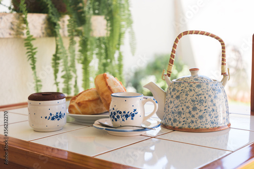 Breakfast served with french bread, tea cup and tea pot on table with sunny background