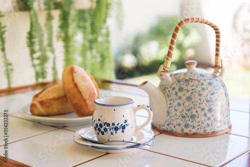 Breakfast served with french bread, tea cup and tea pot on table with sunny background