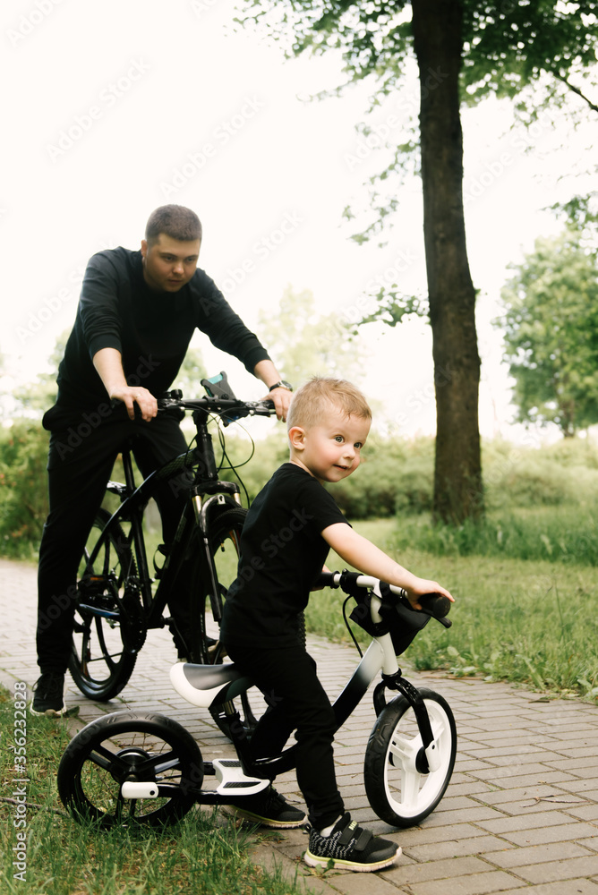Happy little boy rides a bike with a young dad in the Park Happy little boy rides a bike with a young dad in the Park
