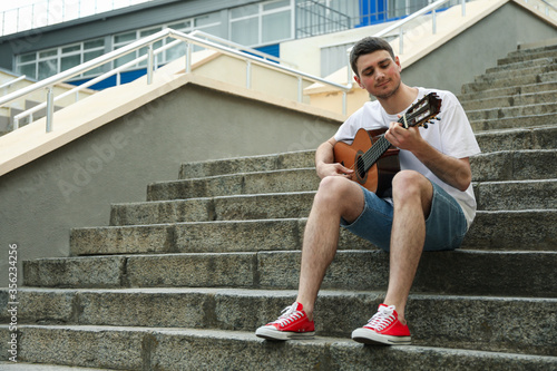Young man sits on the steps and play on guitar © Atlas