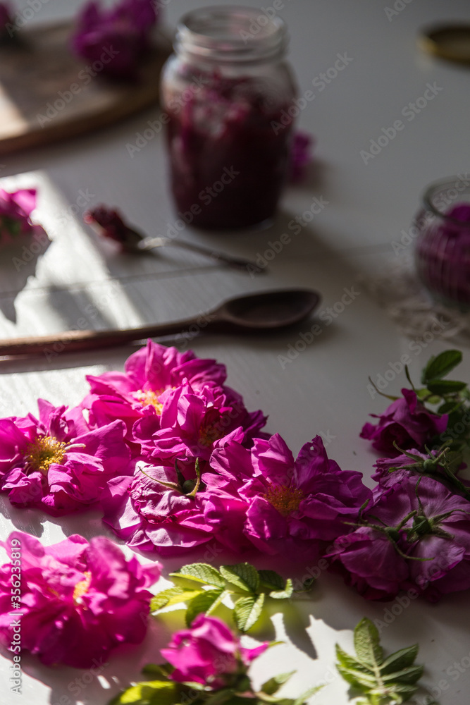 Edible roses with glass jars and spoons on background on white wooden kitchen table . Edible roses with glass jars and spoons on background on white wooden kitchen table .