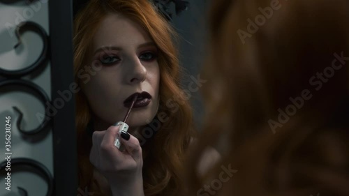 Gothic girl putting on lipstick in front of a mirror