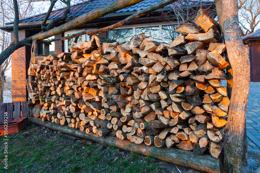 Firewood background. Preparation of firewood for the winter and use for cooking. Stacks of firewood with sun spots.