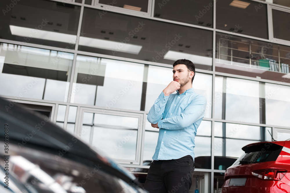 Fototapeta premium Pensive man looks at cars at a auto dealership
