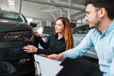 Salesman shows the car to a young client of a car dealership. Girl chooses a new car