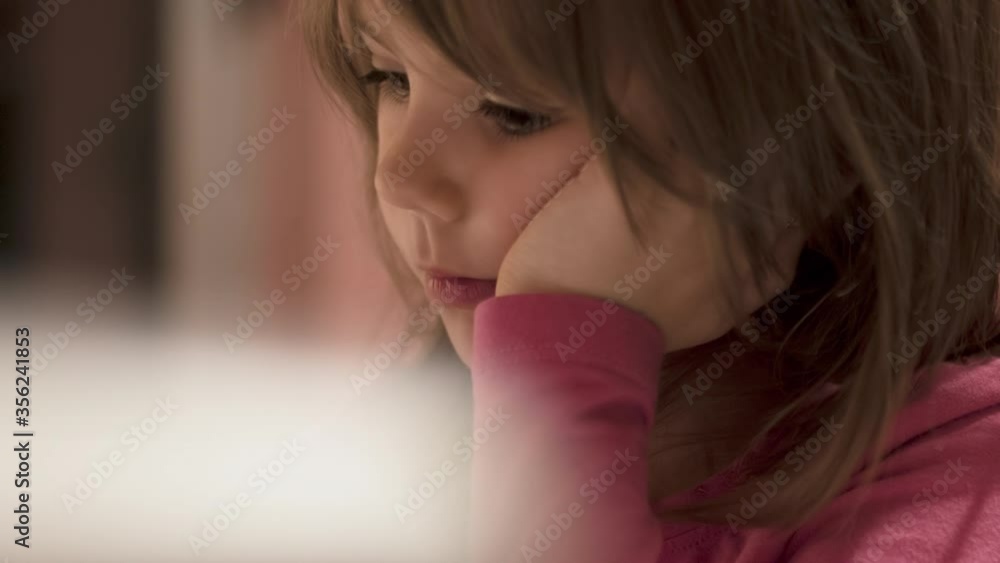 Charming little girl drawing with pencil on her school desk and watching tablet, selective focus Charming little girl drawing with pencil on her school desk and watching tablet, selective focus