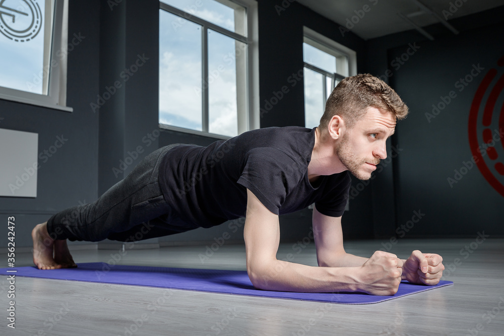 A young man stands in a plank on the elbows in the gym. Men's workout. A young man stands in a plank on the elbows in the gym. Men's workout.