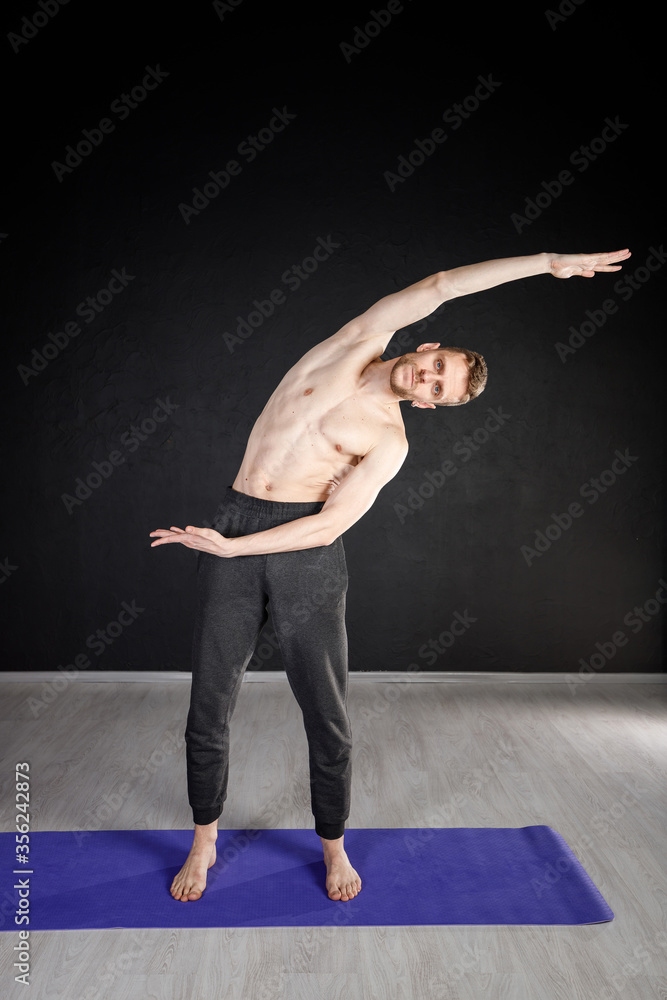 Young man is doing warm-up exercises, stretching his side spine muscles.