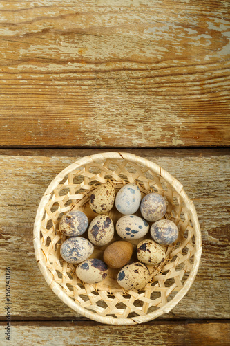 Fresh quail eggs in a wicker basket on a wooden rustic table.
