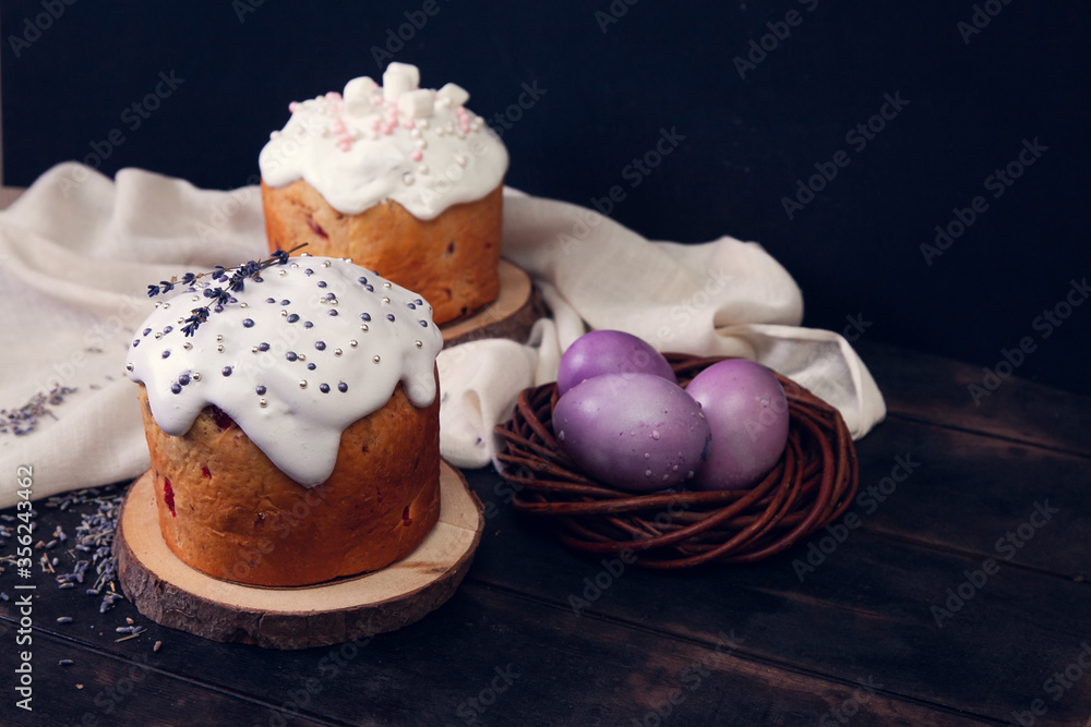 Easter cakes on a dark background, decorated with lavender and marshmallows, and painted Easter eggs in a wicker nest Easter cakes on a dark background, decorated with lavender and marshmallows, and painted Easter eggs in a wicker nest