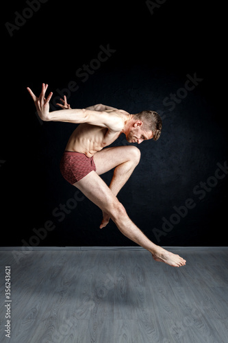Fototapeta Naklejka Na Ścianę i Meble -  Contemporary dance positions. Young man is jumping with his hands behind his back and leg in passe compose.