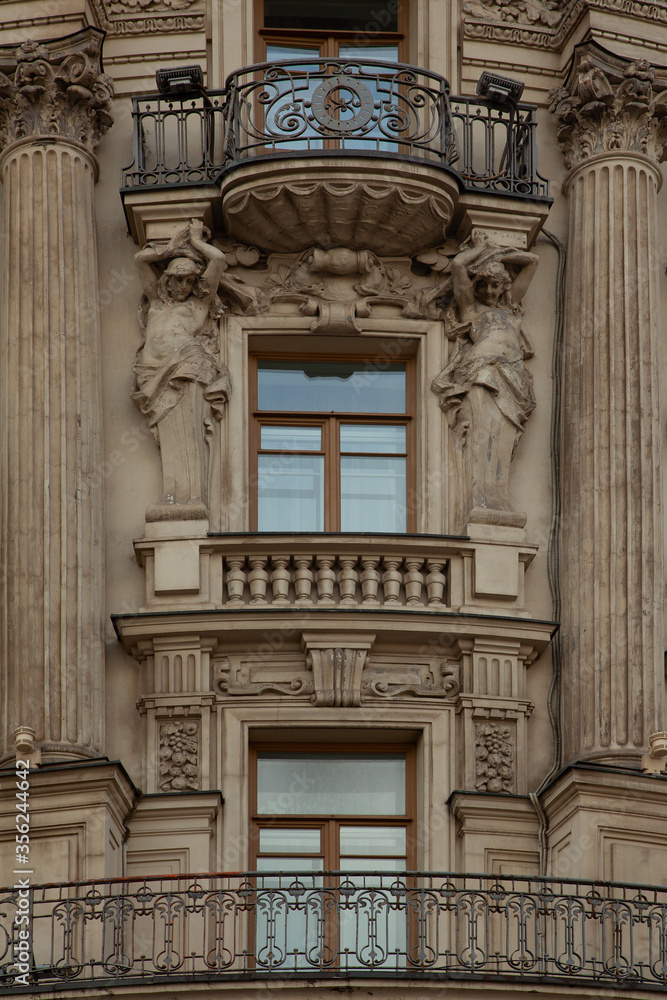 Fragment of the facade of an old building with balconies of an unusual shape, a carved forged fence, stucco molding and sculptures of Atlantes