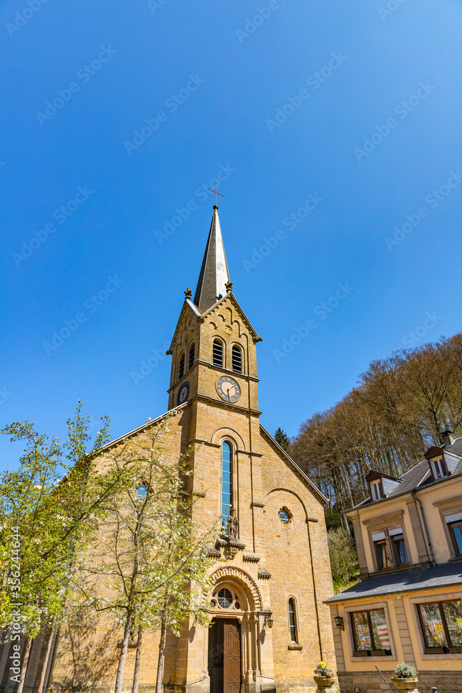 Facade  of Saint Donatus Church and tower with the cross in Larochette, Luxembourg