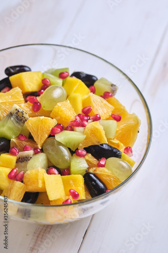 Fruit salad in a transparent glass bowl on a white wooden table.