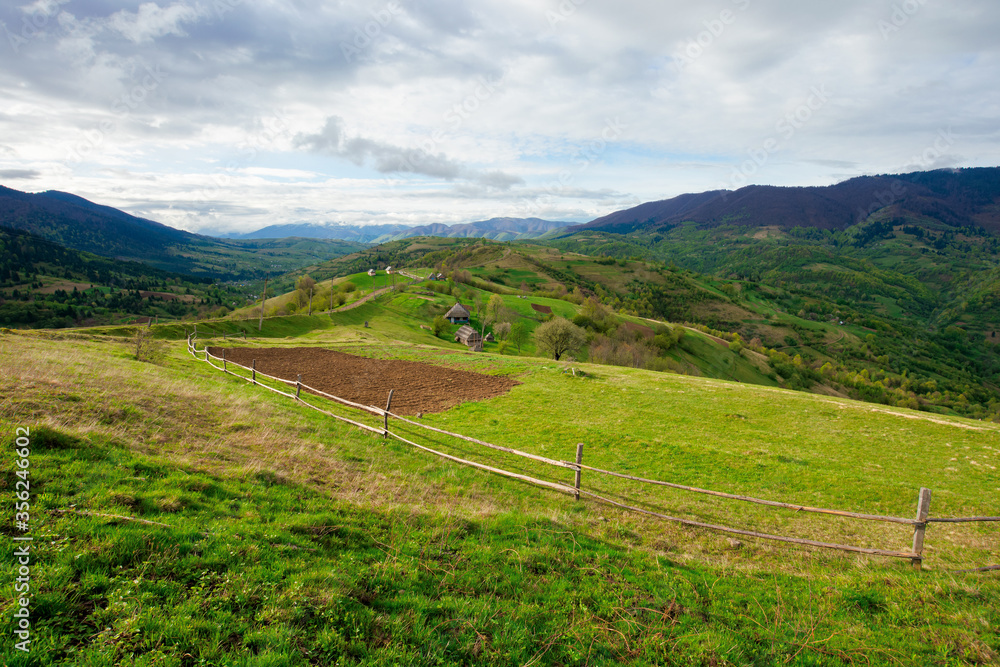 rural fields on mountain hills. beautiful rural landscape of carpathian nature on a cloudy day. path leads to village in the distance. fence across the grassy meadow