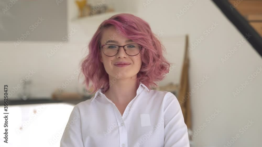 Happy young adult hipster gen z teen girl smiling face with pink hair wearing glasses looking at camera stand in modern kitchen interior. Female small business cafe shop owner entrepreneur portrait. Happy young adult hipster gen z teen girl smiling face with pink hair wearing glasses looking at camera stand in modern kitchen interior. Female small business cafe shop owner entrepreneur portrait.