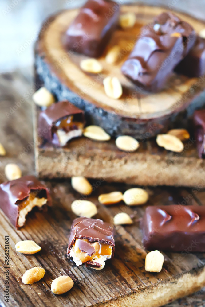 Fototapeta premium Selective focus. Macro. Chocolate bars with peanuts and caramel. Peanut. Wood background. Sweets, chocolate, nuts.