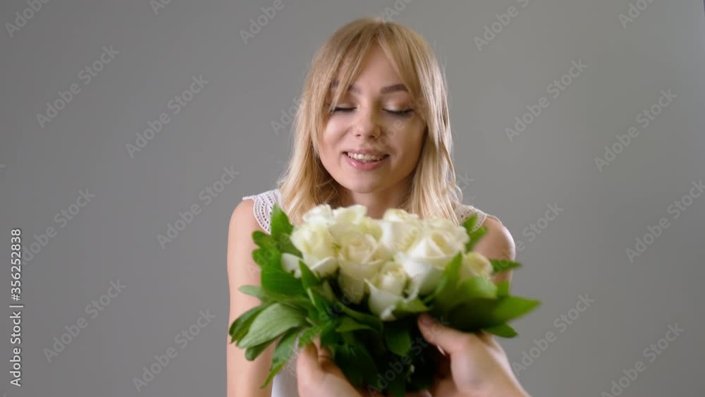 Beautiful young woman receiving bouquet of white roses on grey background Beautiful young woman receiving bouquet of white roses on grey background