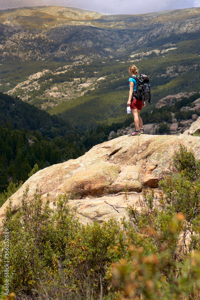 Woman hiking alone, contemplating the view from a rock, with a protective mask in her hand