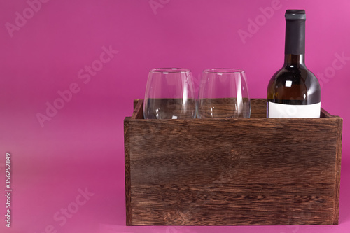 a bottle of wine and two glasses in a wooden box on a pink background