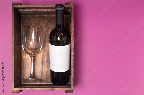 a bottle of wine and a glass in a wooden box on a pink background