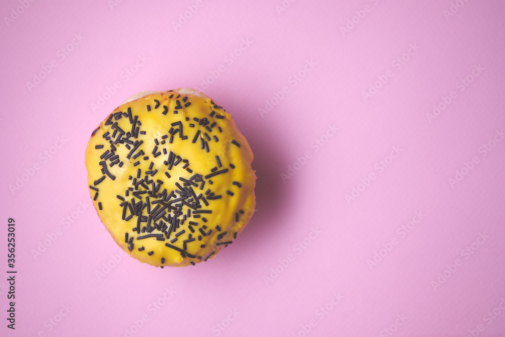 Close-up of a donut with colored glaze on a pink paper background. Top view.