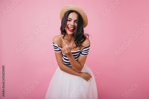 Sensual tanned girl with bright makeup laughing to camera. Indoor portrait of amazing woman in white skirt.