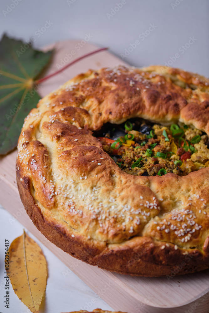 Homemade autumn pie with meat, onions and bell pepper on the board. Dish on a white wooden table. Close-up. Homemade autumn pie with meat, onions and bell pepper on the board. Dish on a white wooden table. Close-up.