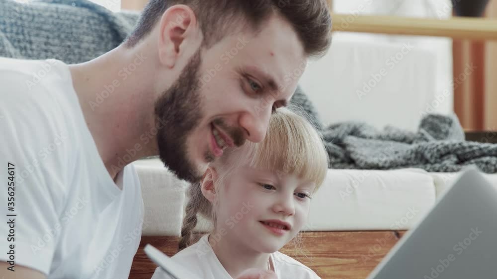 Happy father spending time with his small daughter. They are looking to the notebook Happy father spending time with his small daughter. They are looking to the notebook
