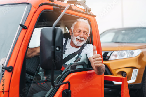 Handsome senior man working in towing service on the road and showing thumb up. Roadside assistance concept.