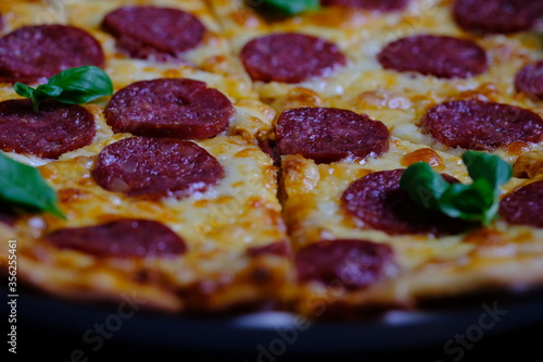 Classic pepperoni pizza with tomato sauce, cheese and salami sausage on a black wooden background.