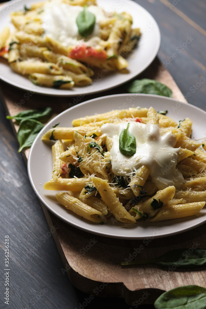 Two portions of pasta with tomatoes, spinach, parmesan and bolognese sauce on a large kitchen wooden board. Dish in a plate on a wooden table. Two portions of pasta with tomatoes, spinach, parmesan and bolognese sauce on a large kitchen wooden board. Dish in a plate on a wooden table.