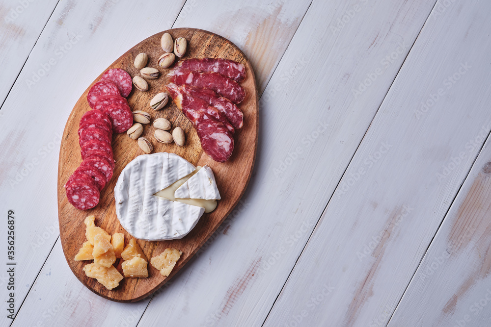 Cheese and sausage delicacies, nuts on a wooden board on an old white table. View from above.