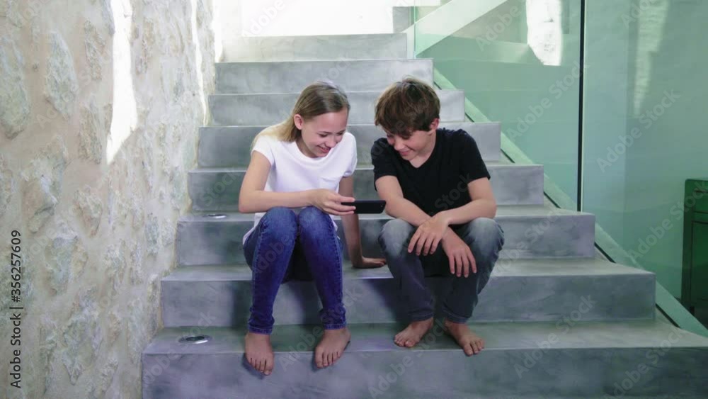 MS Boy (14-15) and girl (12-13) sitting on stairs and using smart phone MS Boy (14-15) and girl (12-13) sitting on stairs and using smart phone