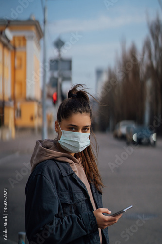 Girl in protective mask using smartphone outdoors. COVID 19. World coronavirus pandemic.