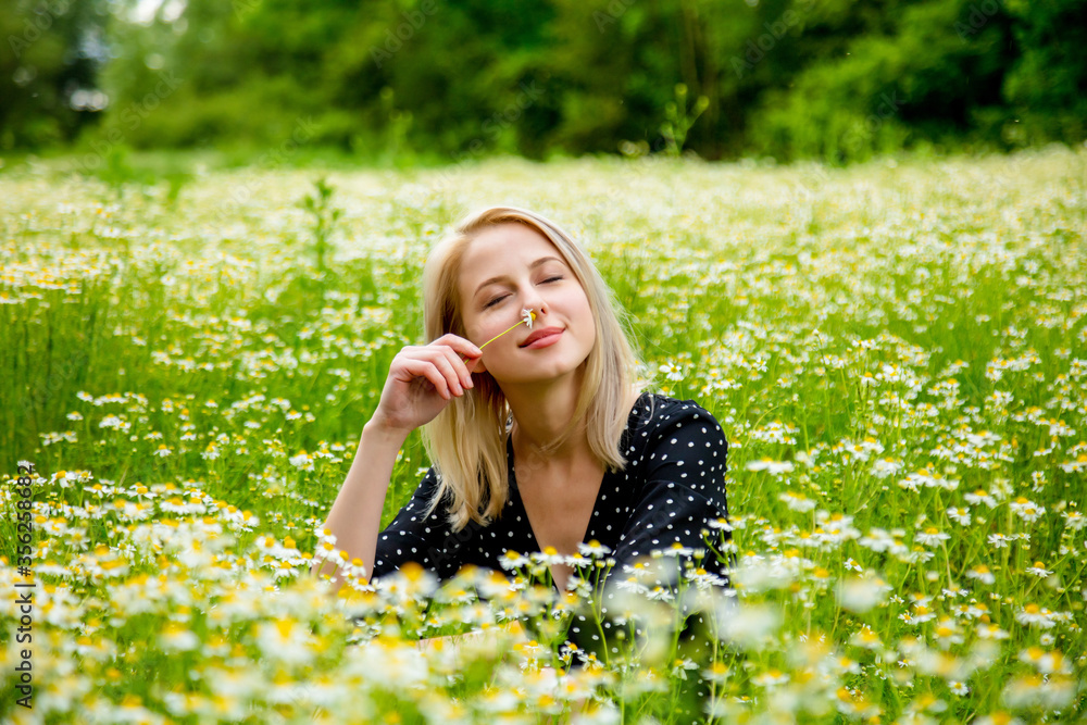 Blonde woman in black dress is sitting in countryside chamomiles flowers field Blonde woman in black dress is sitting in countryside chamomiles flowers field