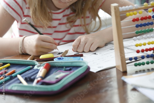 Kleines Mädchen Grundschule, Lernen, Hausaufgaben machen, Schreibtisch zuhause, rechnen mit Abacus Rechenschieber, mit Mäppchen Stifte, close-up. photo