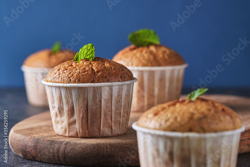 Fototapeta Naklejka Na Ścianę i Meble -  Lemon muffins with poppy seeds, decorated with mint, on a wooden board. Background color classic blue.