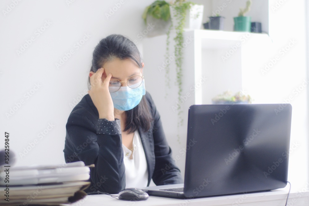 Mujer de negocios con máscara preocupada frente a su computadora. Joven ejecutiva con máscara pensativa por la crisis económica a causa de la pandemia por COVID 19. Mujer de negocios con máscara preocupada frente a su computadora. Joven ejecutiva con máscara pensativa por la crisis económica a causa de la pandemia por COVID 19.