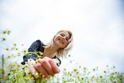 Canvas Print Low poit of view as blonde woman is plucking a chamomiles flower