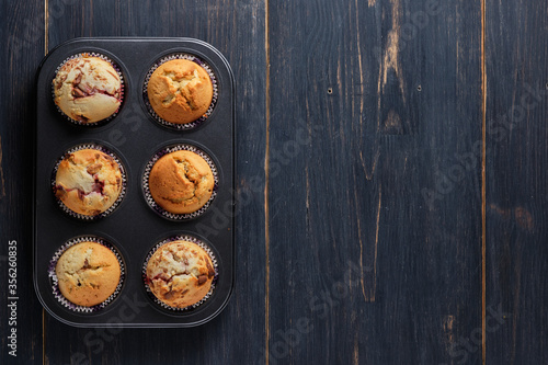 A composition of berry-chocolate muffins in a baking dish on an old wooden table. View from above. Place for text.