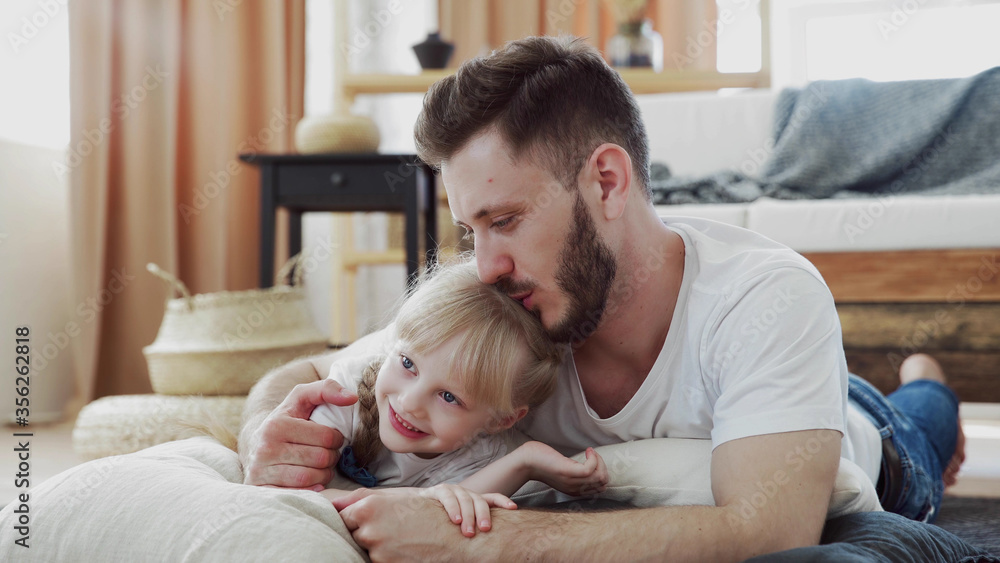 Loving father hugging and kissing his daughter on the floor. Happy child and daddy feeling joyful. Handsome dad and his cute little girl embraces together, shares love on Father Loving father hugging and kissing his daughter on the floor. Happy child and daddy feeling joyful. Handsome dad and his cute little girl embraces together, shares love on Father