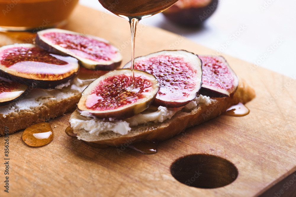 Bruschettas with figs, soft cheese and honey on a wooden board.